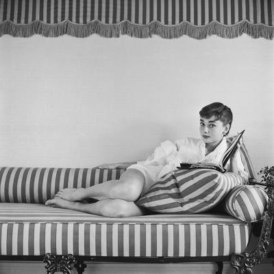 Mark Shaw Mark Shaw AUDREY HEPBURN ON STRIPED SOFA RECLINES BOOK OPEN 1954