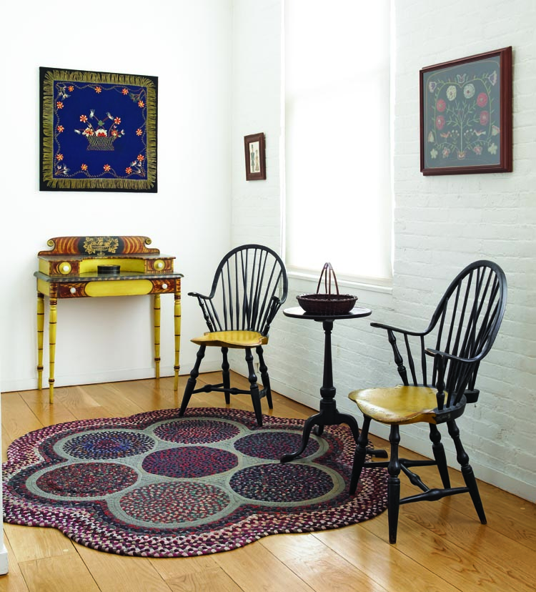The collectors like unconventional pieces, such as the pair of late-18th-century Rhode Island braceback Windsor side chairs with vivid yellow seats. Elliott Snyder attributes the circa-1825 stepback dressing table with double-amphitheater back to Martin Bullock (1810–1876) of Newport, New Hampshire. The dressing table was deaccessioned from the Hitchcock Museum in Connecticut. A similar piece is in the New Hampshire Historical Society. The Rhode Island dish-top candlestand dates to circa 1780–90. It is topped with a circa-1900 Taghkanic “friendship” basket. The circular flower hooked rug came from Judith and James Milne Antiques in New York City.
