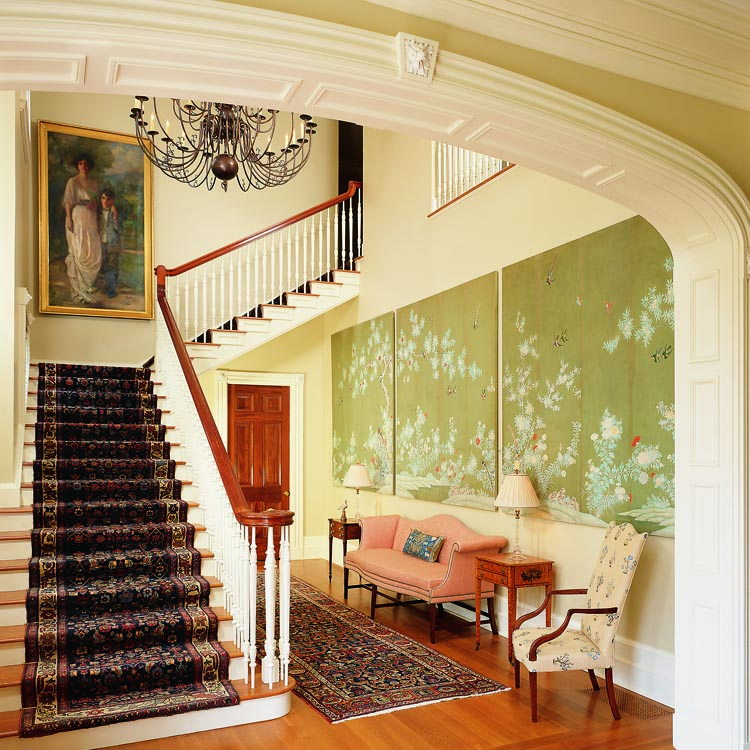 A family portrait of the Virginia-born wife’s grandfather and great-grandmother greets visitors from the top of the stairs. The couple commissioned 100 banisters in the style of Samuel McIntire, their favorite carver, to support the stair rail. The husband discovered the Dutch chandelier in Argentina. Mounted as three panels, the hand-painted Chinese wallpaper came from Taylor Williams Antiques. The two circa 1890 Bidjar stair runners are from Oriental Rugs, Ltd., in Old Lyme, Ct., as is the circa 1900 Kurdish rug by the sofa. Wayne Pratt Antiques supplied the nineteenth century New York camelback sofa and the Boston Federal work table, right, attributed to John and Thomas Seymour.