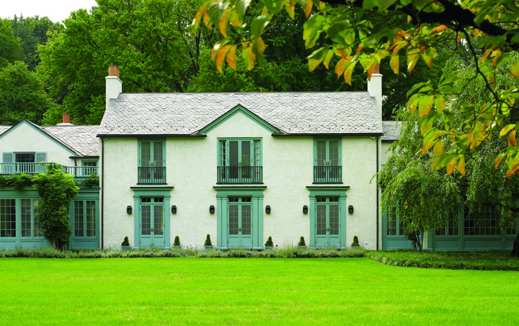 The northwest façade of the house, which was probably once a carriage barn on this former estate property, presents as a country manor house, thanks to new French doors, iron balconies, and trim painted a well-mannered antique blue.