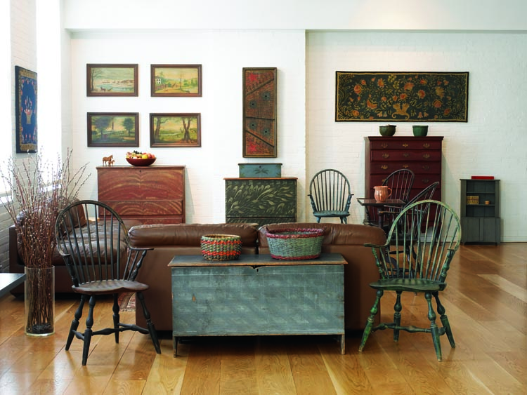 “We made living with antiques a priority,” says the wife. Postponing renovations to their country house, the couple recently splurged on a circa-1830 pine chest-over-drawer, center rear, possibly from Rhode Island. Above it, a circa-1890 hammer dulcimer in an exuberantly painted case is attributed to Reuben Matheny of Ritchie County, West Virginia. The circa-1800 blanket chest in the foreground features original blue paint and incised decoration. The New York continuous-arm, ca. 1795, Windsor chair is branded “J. Sproson.”