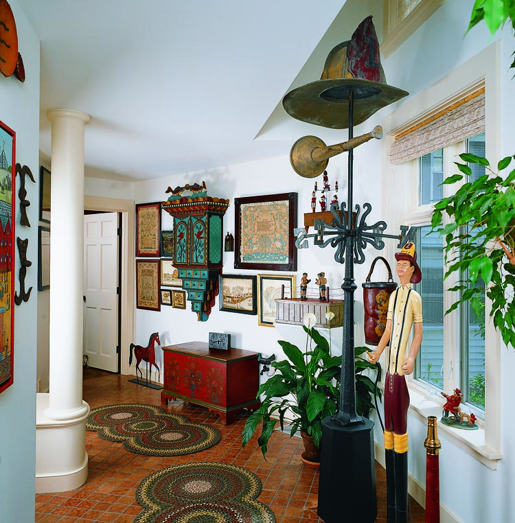 The most prominent object in the hallway is the 76-inch-high fireman’s helmet and horn weathervane with cast-iron flame directionals attributed to J.W. Fiske. Discovered on a Maine firehouse by Robert Bishop, it was exhibited in 1993 at the American Folk Art Museum in celebration of the opening of the Bishop wing. The couple commissioned the 1993 carving of the fireman, placed beside the firehouse weathervane, from Kentucky artist James Allen Bloomfield. Further down the hall is a pair of carved wooden boxers from the Barenholtz collection. They were given to toymaker Louis Marx, who, in 1938, used them as prototypes for his “Rock-em, Sock-em Robots” game. Needlework samplers from Mary Balch’s school in Providence, Rhode Island, Miss Patten’s School in Hartford, Connecticut, Newburyport’s Byfield Academy, and a number of schools in Pennsylvania, flank the carved 1987 hanging cabinet by Vermont artist Stephen Huneck (b. 1948). Below it is a painted blanket chest from 1830 by Joel Palmer of Fulton County, Pennsylvania, with initials for Henry Stoner. It descended in the Stoner family until purchased by Olde Hope Antiques and subsequently sold to the collectors. An 1890s horse silhouette weathervane is from Sam Herrup.