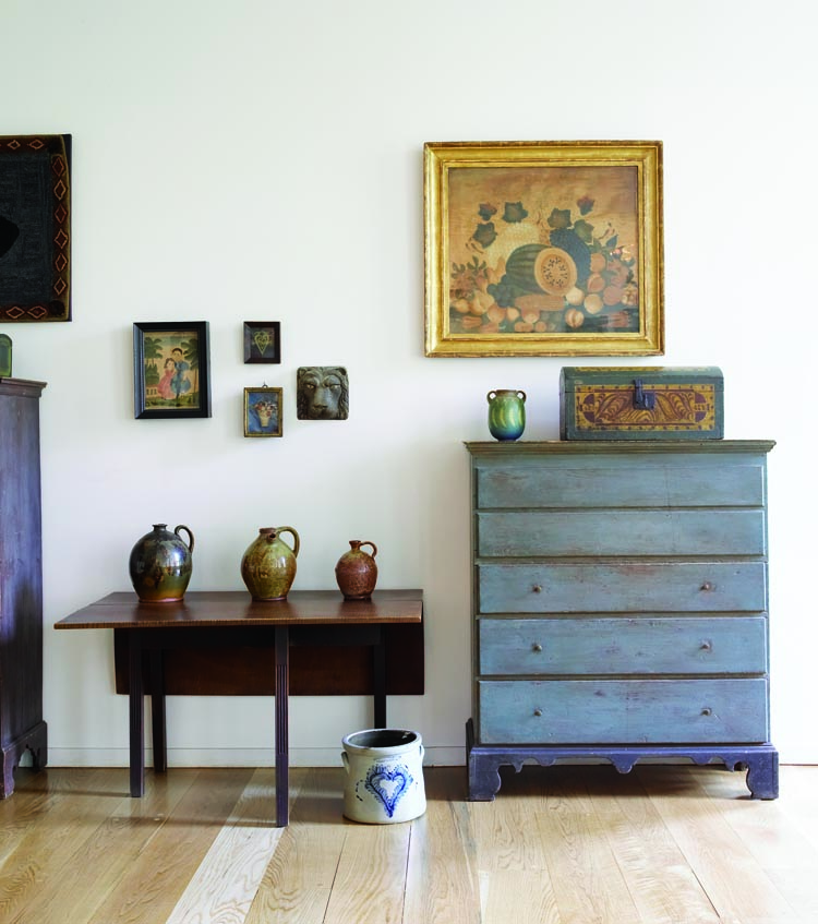 The blue-green lift-top blanket chest, located by the sitting area, is possibly from North Shore, Massachusetts; it was the husband’s first piece of American furniture. The 18th-century Rhode Island drop-leaf dining table has stop-fluted legs and old or original surface. On it is arrayed circa-1840 New England redware, including a Maine harvest jug, center, that came from John Keith Russell, Purchased from Old Hope Antiques, the circa-1830 theorum painting on velvet combines stenciled and freehand decoration. Decorated in cobalt with a heart and stamped “Seymour & Bosworth, Hartford,” the Connecticut crock was a Valentine’s Day gift from the wife to her husband.