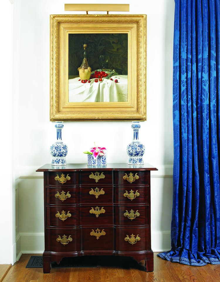 Above an eighteenth- century Massachusetts Queen Anne block-front chest hangs Still Life with Wine and Strawberries, signed and dated 1872 by Milne Ramsey (18447–1915) and purchased from MME Fine Art. It is one of several still life paintings that evoke a “life imitates art” sensibility in the dining room. Ramsey spent most of his career in Philadelphia and also lived for a short time in New York, earning a reputation as a still life, plein-air landscape and portrait painter. A trompe l’oeil approach distinguishes Ramsey’s still lifes, as seen here in his depiction of the table linens, bottle, bowl, and berries. Atop the chest are a pair of eighteenth-century Dutch Delft “garlic” vases and an English Delft
