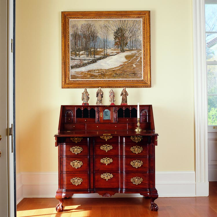 This Chippendale mahogany block-front, slant-front desk from Salem, Massachusetts, circa 1750–1770, features cast-brass pulls and escutcheons with phoenix-bird crowns. The four eighteenth-century carved, gessoed , painted, and gilded figures of saints are Brazilian. The 1912 painting by Samuel Harkness McCrea is one of two McCrea canvases in the couple’s collection, both from the artist’s estate.