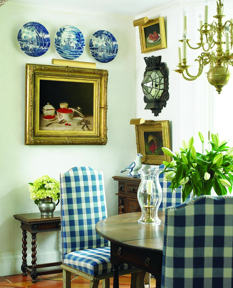 The kitchen’s light-filled dining alcove derives its comfortable Continental ambiance from an array of eighteenth-century furnishings, which include an English drop-leaf table, a small, heavily carved Italian chest and table, chairs upholstered in a blue and white “furniture check,” a brass chandelier that is either English or American, a French sconce, Dutch Delft ceramics, and a large French faience bird. The focal painting is a still life with raspberries and a pitcher of milk by John F. Francis (1808–1886). “It’s one of my favorite paintings, and in this spot, I get to look at it every day,” the wife says. The small painting below the sconce is a George Henry Hall still life of raspberries spilling from a basket, typical of the naturalistic style of the era; both were purchased from Godel & Co. Above the Hall canvas hangs a still life with peaches, painted by George Harvey (1800–1878), who designed Sunnyside, the Hudson River home of his best friend, author Washington Irving.