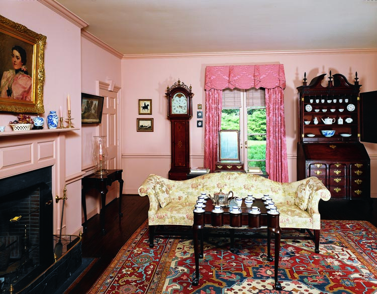 Against the back wall of the guest sitting room is one of three known tall clocks with a case by Sutton, Mass., cabinetmaker Nathan Lombard (1777–1847). Along the same wall is a secretary block-front bookcase attributed to Boston cabinetmaker George Bright (1726–1805). It descended in the family of General Arad Hunt. Its shelves contain part of the twenty-piece porcelain tea service with the monogram of Abigail Adams, purchased for her by her husband, John Adams. The rare Boston turret-top table in the center of the room is one of six known examples. Behind it is a sofa from the Meyer collection. Beside the fireplace is a rare diminutive turret-top Boston Queen Anne card table, one of two flanking the fireplace.