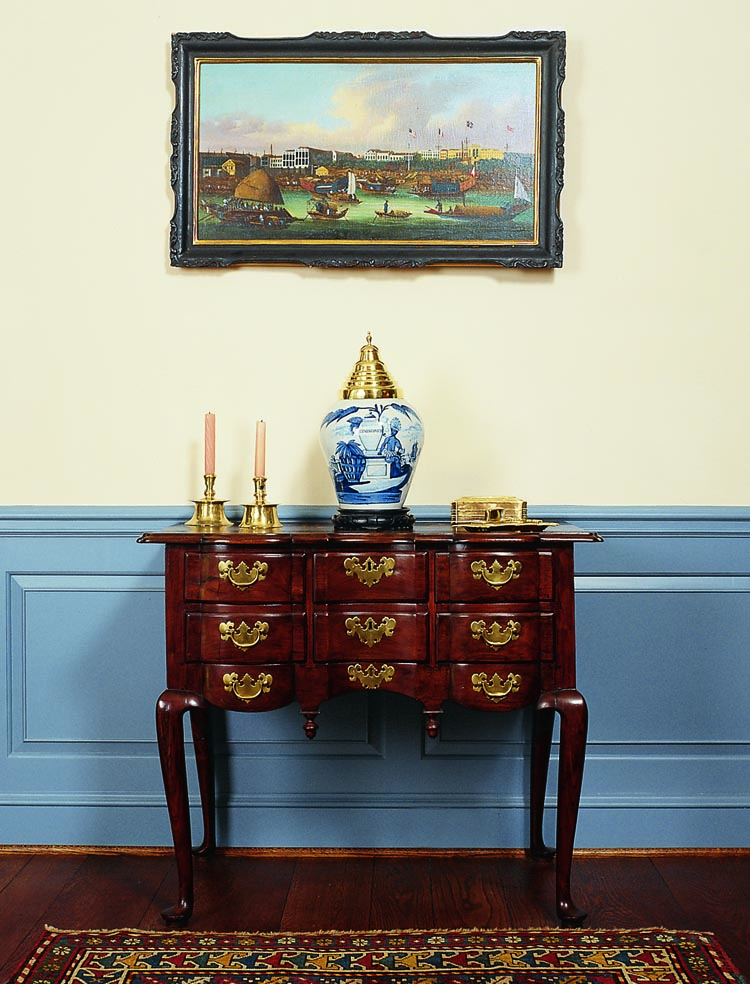 This dressing table is one of only seven of its type known. It features rounded blocking on the façade and a row of brass hardware on the skirt intended to simulate a third row of drawers. Others from this unidentified shop are in the Museum of Fine Arts, Boston, Winterthur, and The Metropolitan Museum of Art. Purchased from the Merriam family, it was originally owned by Josiah Merriam (1726–1809) of Concord, Mass. The Merriam’s were among the first group of settlers who founded the town in 1635, and some of the skirmishing during the Battle of Concord took place on Josiah's property. Above it hangs a China trade painting, circa 1840, of the Canton Factories; it retains its original frame. The blue and white delft, circa 1700, includes a large tobacco jar with brass lid.